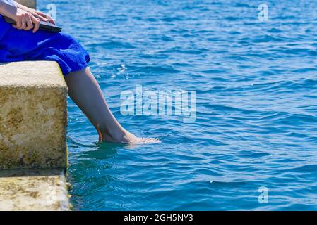 Work from anywhere. Side view of young woman, female freelancer in straw hat working on laptop while sitting on the beach. young woman working Stock Photo