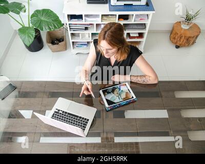 From above of female graphic designer using netbook and tablet with stylus while working on project at table in creative studio Stock Photo