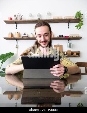 Content male designer drawing on graphic tablet with stylus while sitting at table in creative studio and working on project Stock Photo