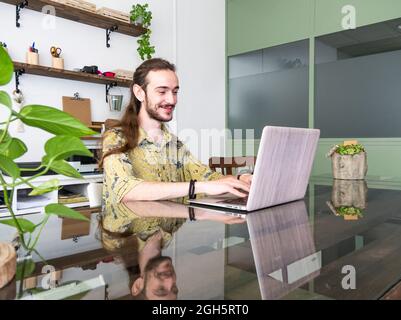 Delighted nape with long hair typing on netbook while working on project in modern creative workspace Stock Photo