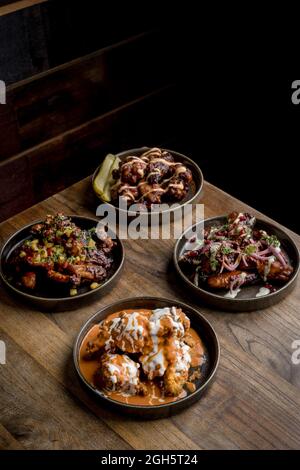 High angle of appetizing crispy chicken with sauces placed near plated with chicken wings in BBQ sauce served with vegetables on wooden table in resta Stock Photo