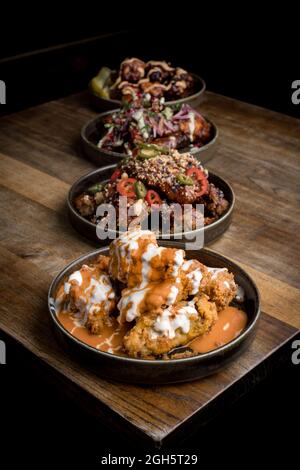 High angle of appetizing crispy chicken with sauces placed near plated with chicken wings in BBQ sauce served with vegetables on wooden table in resta Stock Photo