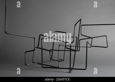 Black and white abstract tangled sculpture made of metal tubes with smooth surface on gray background Stock Photo