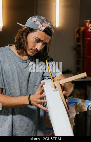 Concentrated male hipster using scribe tool with pencil while marking surfboard before shaping in workshop Stock Photo