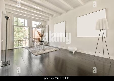 Modern loft home interior design with dining table and chairs placed near window in corner of spacious room with mockup pictures hanging on white wall Stock Photo