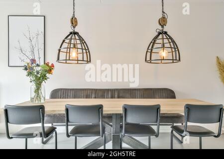 Elegant interior design of modern dining room with chairs and sofa placed near wooden table with bouquet of flowers under glowing lamps with metal ele Stock Photo