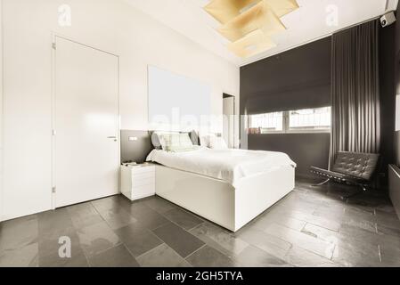 Spacious light bedroom with queen size bed and attached bathroom in modern loft style apartment with white walls and marble floor Stock Photo