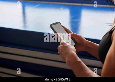 Side view of crop unrecognizable female athlete in bra surfing Internet on mobile phone with empty screen in gym Stock Photo