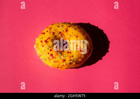 Top view of one donuts coated with a yellow sugar with colored balls on pink background Stock Photo