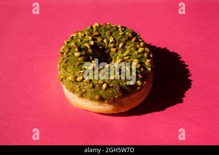 Top view of one donuts coated with a green sugar with nuts on pink background Stock Photo