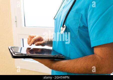 Anonymous male medic in uniform and with stethoscope standing in hospital and surfing Internet on tablet Stock Photo