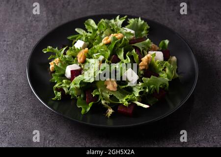 High angle of black plate with tasty beetroot salad with Tofu cheese and green lettuce served on dark background in studio Stock Photo