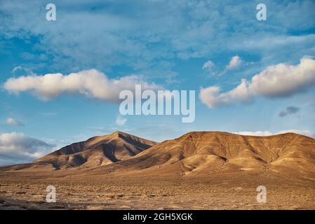 White clouds floating on bright blue sky over arid valley and hills on summer day in Fuerteventura, Spain Stock Photo