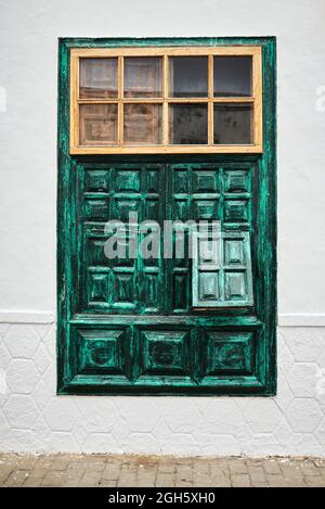 Unconventional window with ornamental green shutters located on white building wall on town street Stock Photo