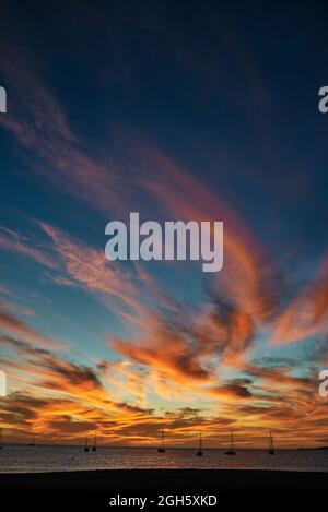 Sundown sky with vivid orange clouds located over sea water with boats in evening in Fuerteventura, Spain Stock Photo