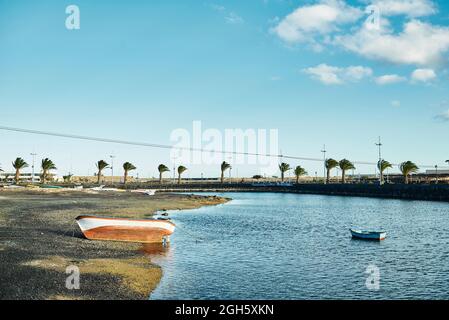 Shabby vessels located on grungy coast and rippling river water on windy day in Fuerteventura, Spain Stock Photo