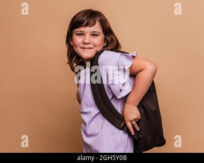 Cute schoolchild standing on brown background in studio and looking at camera Stock Photo