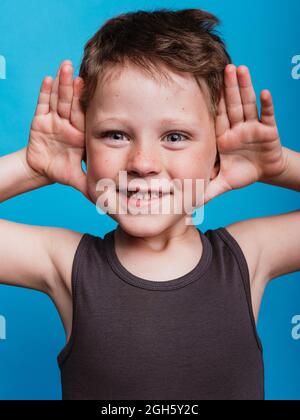 Joyful preteen boy with open palms near face expressing happiness in studio on bright blue background Stock Photo