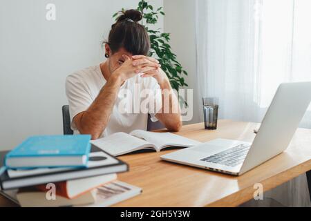 Pensive student making notes from laptop. Young man studying at home and prepare for pass exam Stock Photo