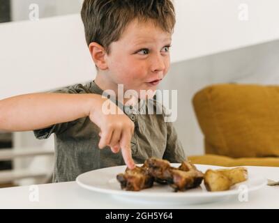 Positive child sitting at table with plate with meat and having tasty lunch in kitchen at home Stock Photo