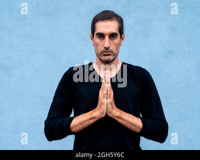 Serene ethnic male standing in prayer hands on the street and practicing yoga Stock Photo