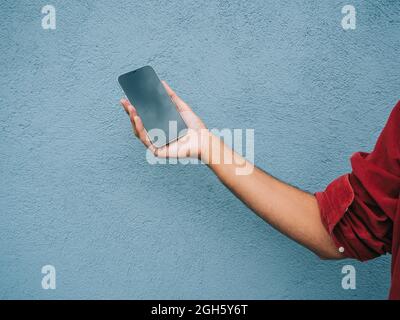 Crop unrecognizable male showing modern mobile phone with black screen on blue background in city Stock Photo