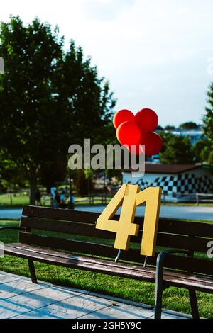 Red balloons and number 41 on bench during birthday party in town on sunny day Stock Photo