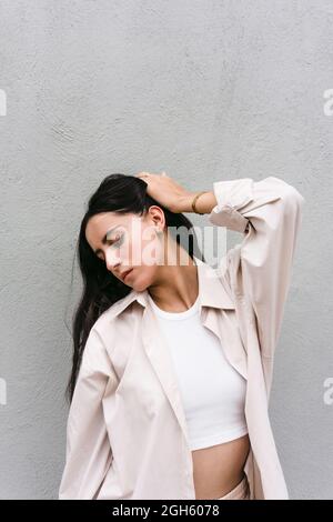 Talented contemporary female dancer posing with hand on head against concrete wall in urban area in city Stock Photo