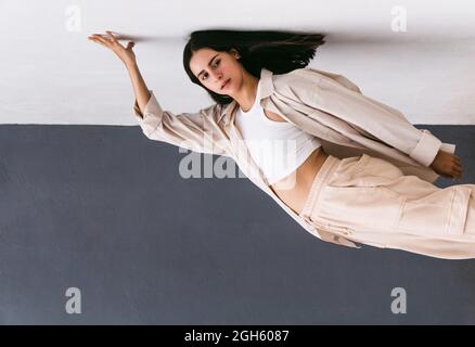 Carefree creative dancer performing in city street and leaning on wall while showing backbend and looking away Stock Photo