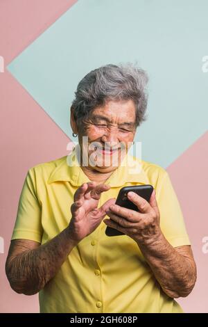 Delighted modern senior female with gray hair browsing social media on mobile phone on two colored background in studio Stock Photo