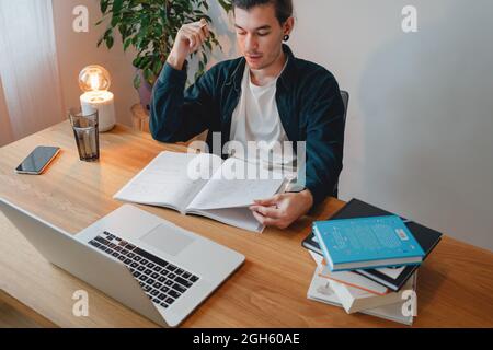 College student preparing for pass exam at home. Young man making notes while online learning Stock Photo