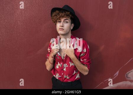 Young stylish homosexual man in ornamental shirt and hat with long nails and tattoo looking at camera Stock Photo