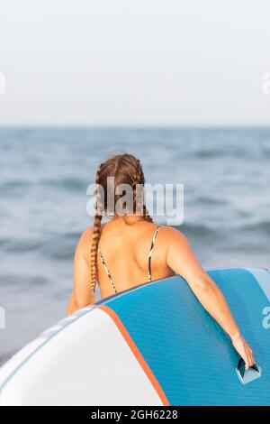 Young positive female in fashionable sunglasses and bright orange knitted cardigan standing near stairs and blue wall Stock Photo