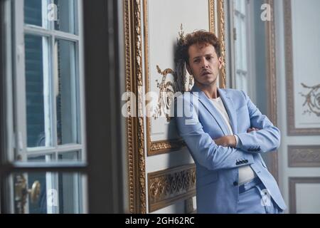Thoughtful male in suit standing with crossed arms and leaning on wall in posh room Stock Photo