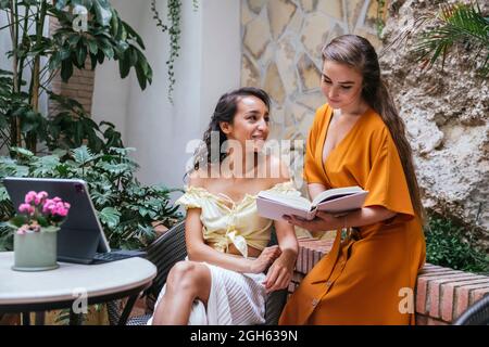 Multiracial female freelancers sitting at table in tropical cafe and working on project while typing on keyboard dock of tablet Stock Photo