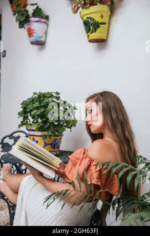 Full body of positive African American female with paper bag of greens eating apple and looking at camera while standing near building Stock Photo