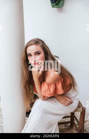 High angle of serene female with red lips and long hair leaning on hand while chilling in patio in summer and looking at camera Stock Photo
