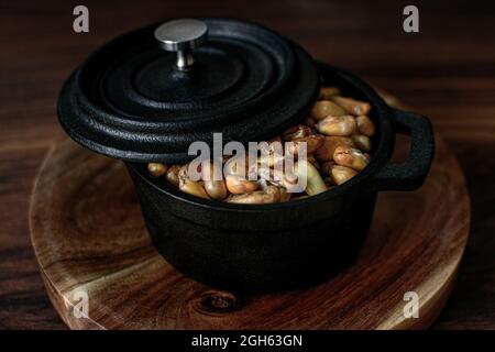 High angle of heap of cereal grain in black saucepan with lid placed on wooden board on table in kitchen Stock Photo