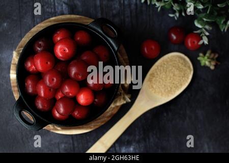 Top view of bowl with fresh sweet plums served on black table with wooden spoon with sugar Stock Photo