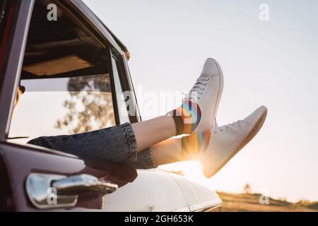 Side view of crop female chilling in vintage car with legs sticking out of window in evening in nature Stock Photo