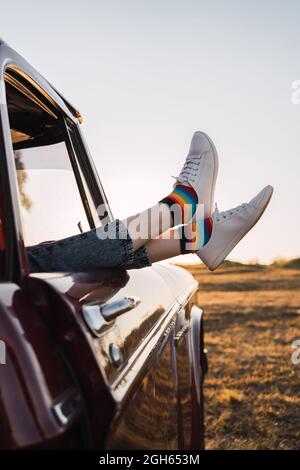 Side view of crop female chilling in vintage car with legs sticking out of window in evening in nature Stock Photo