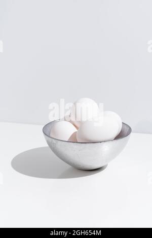 Bowl with fresh chicken eggs placed on table on white background in studio Stock Photo