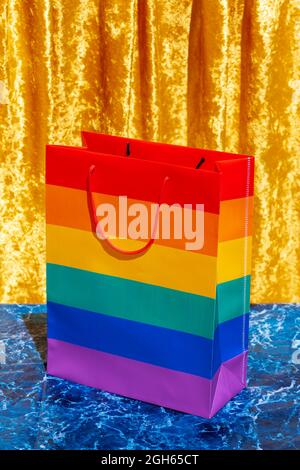 Paper shopping bag with LGBT rainbow flag placed on table in studio on blue and yellow background Stock Photo