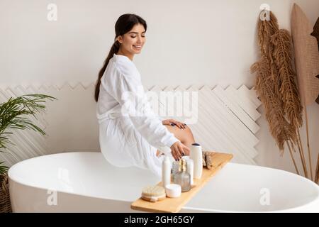 Female Choosing Cosmetics On Shelf Caring For Body In Bathroom Stock Photo