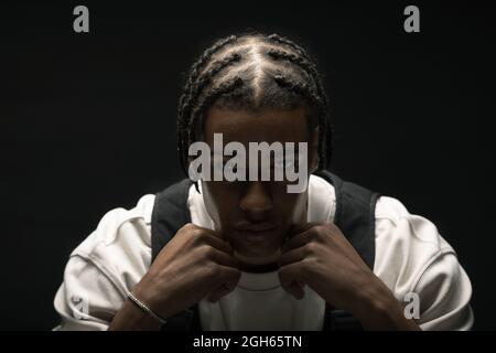 Serious young African American male model with braided hairstyle wearing stylish outfit looking at camera against black background Stock Photo