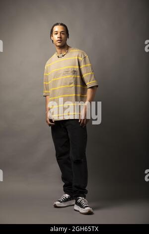 Young African American male model with braided hair dressed in oversized striped shirt and necklace looking at camera against gray background Stock Photo