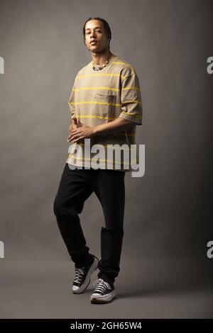 Young African American male model with braided hair dressed in oversized striped shirt and necklace looking at camera against gray background Stock Photo