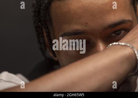 Headshot of serious young African American male with braided hair and bracelet on wrist looking at camera thoughtfully Stock Photo