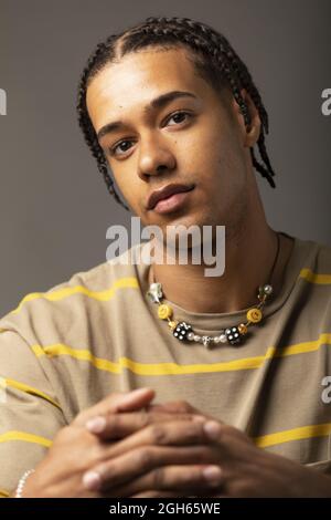 Young African American male model with braided hair dressed in oversized striped shirt and necklace looking at camera against gray background Stock Photo