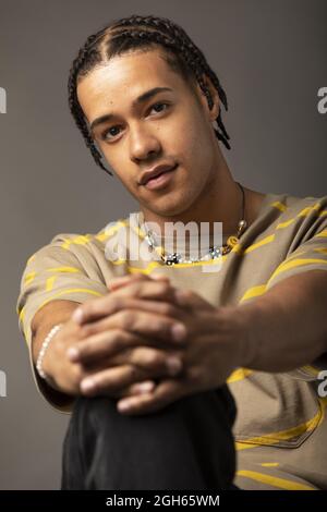 Young African American male model with braided hair dressed in oversized striped shirt and necklace looking at camera against gray background Stock Photo